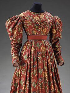 Šaty z roku 1830, ušité z květované bavlněné látky. Na potisk materiálu byla zřejmě použita barviva z mořeny barvířské a indiga. Při detailním pohledu (další fotografie a popis šatů jsou dostupné na stránkách Viktoriina a Albertova muzea) jsou patrné tehdy časté tiskové chyby, hlavně špatné sesazení jednotlivých barev.